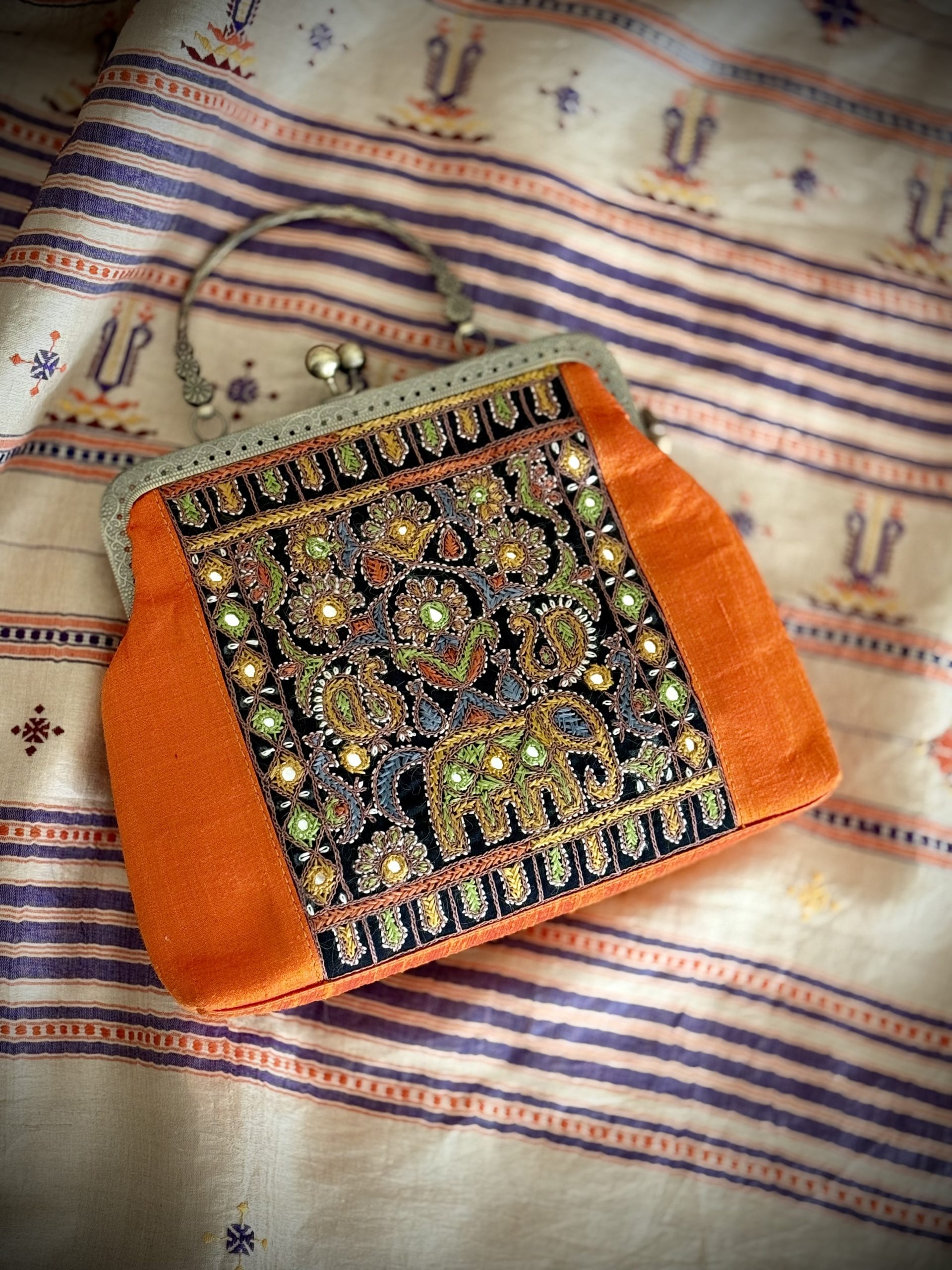 Orange Kutchi embroidered handbag photographed at an angle